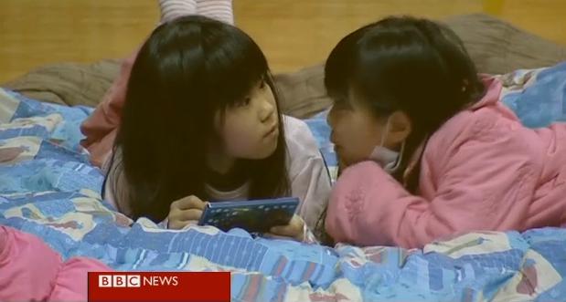  Two young girls play on a Nintendo DS while in a emergency shelter 50km north of  Fukushima.